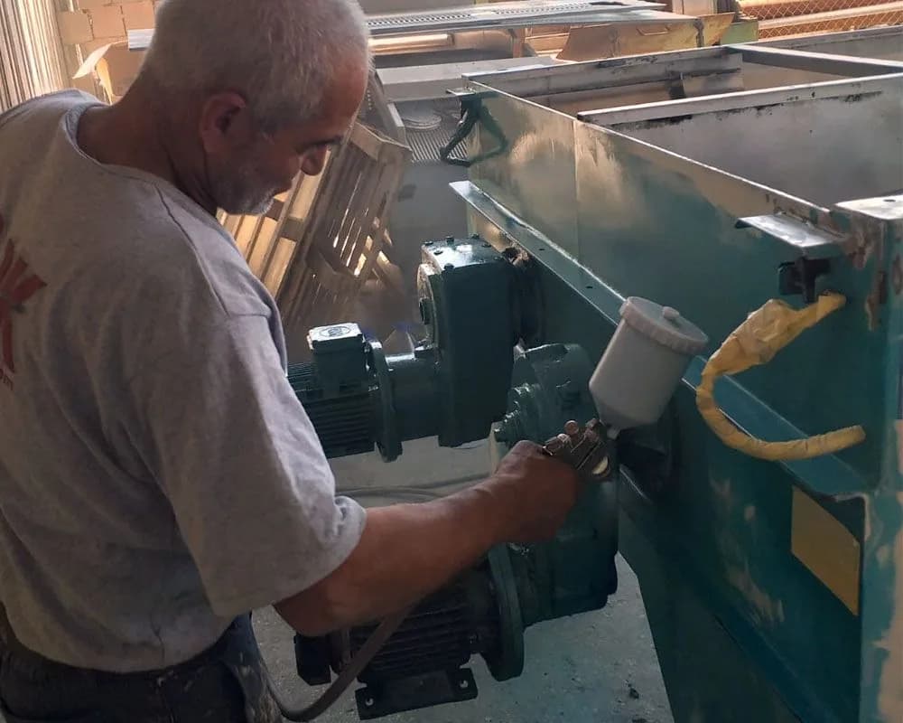 Kasacı Mustafa Usta atölyede boya tabancasıyla endüstriyel bir makinenin gövdesini boyarken